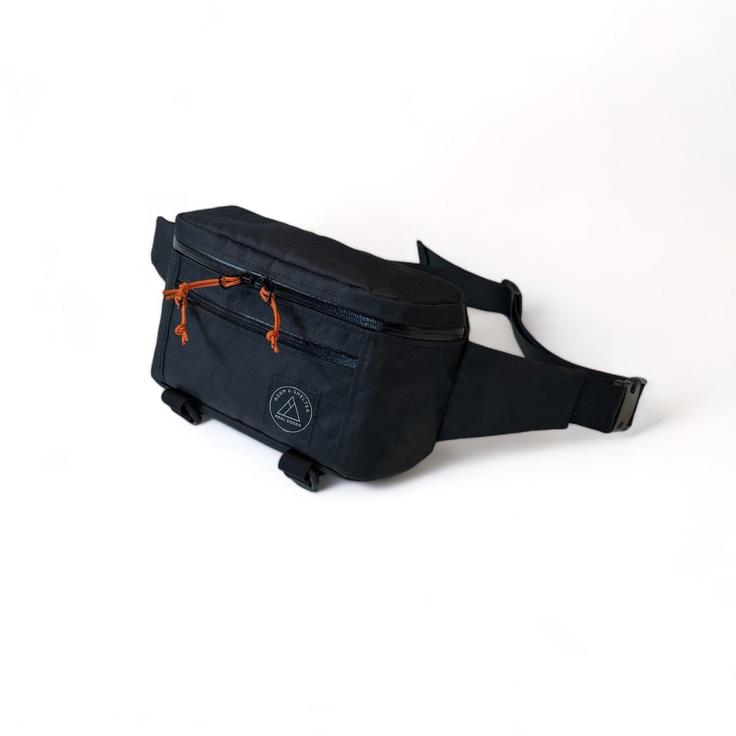 A black hip pack with dual zipper main compartment, external front pocket, and an adjustable strap. It features orange zipper pulls and additional straps for jacket storage. Handmade in Portland Oregon USA.