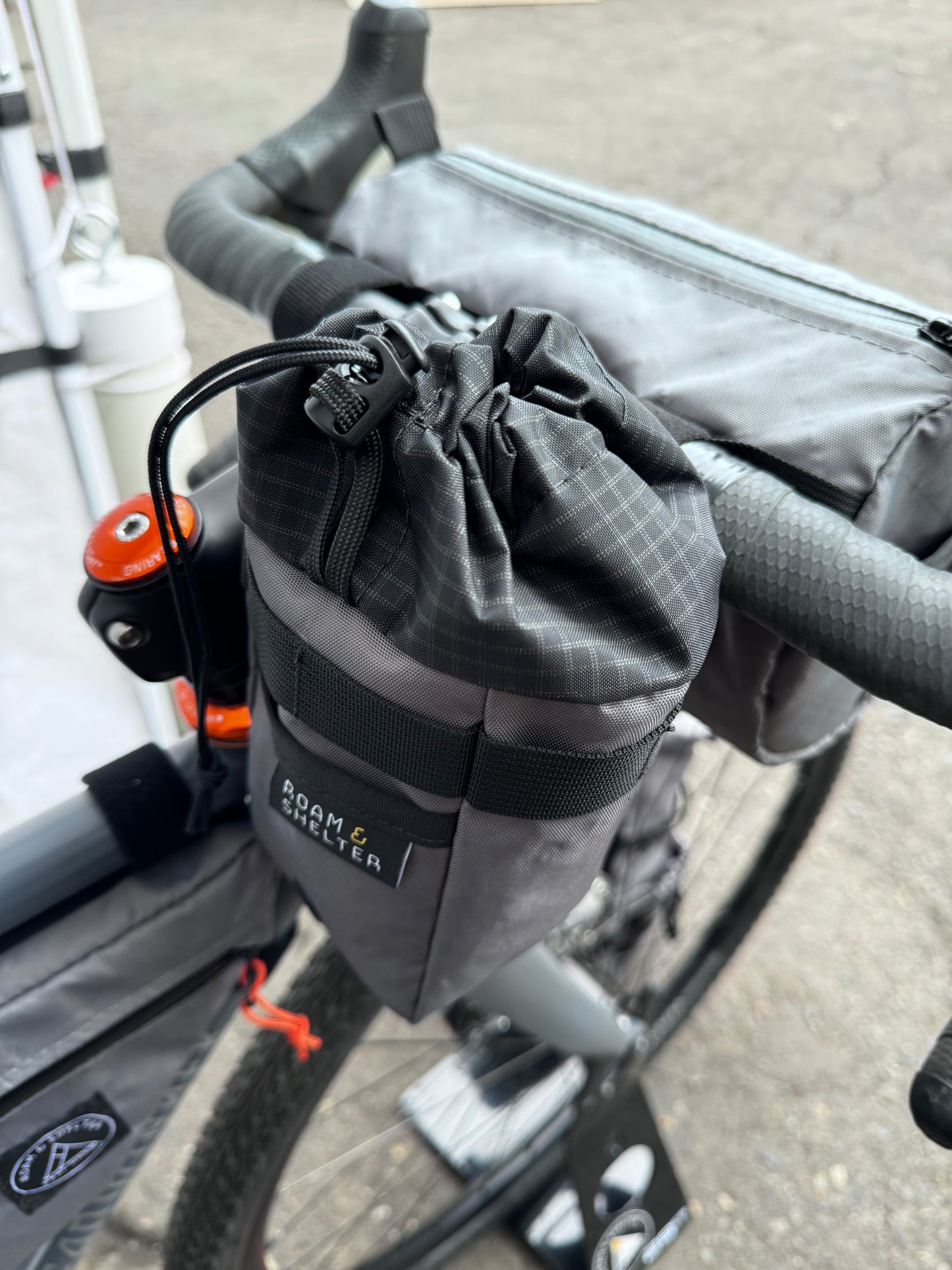 A gray stem bag attached to a bicycle's stem and handlebar, featuring a drawstring closure and made of Ecopak 400 material.  Two external pockets.  Handmade in Portland Oregon USA.