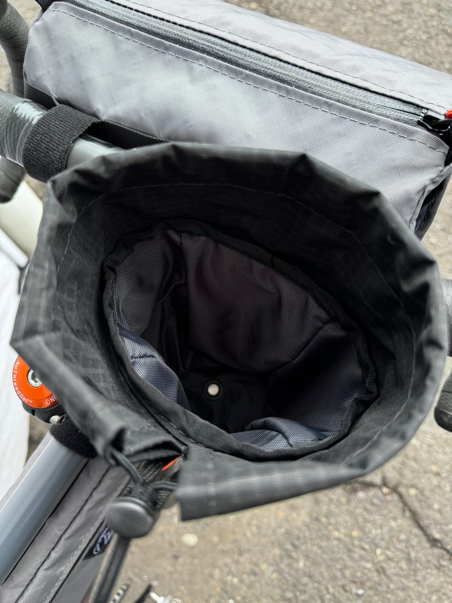A gray stem bag attached to a bicycle's stem and handlebar, featuring a drawstring closure and made of Ecopak 400 material.  Two external pockets.  Handmade in Portland Oregon USA.