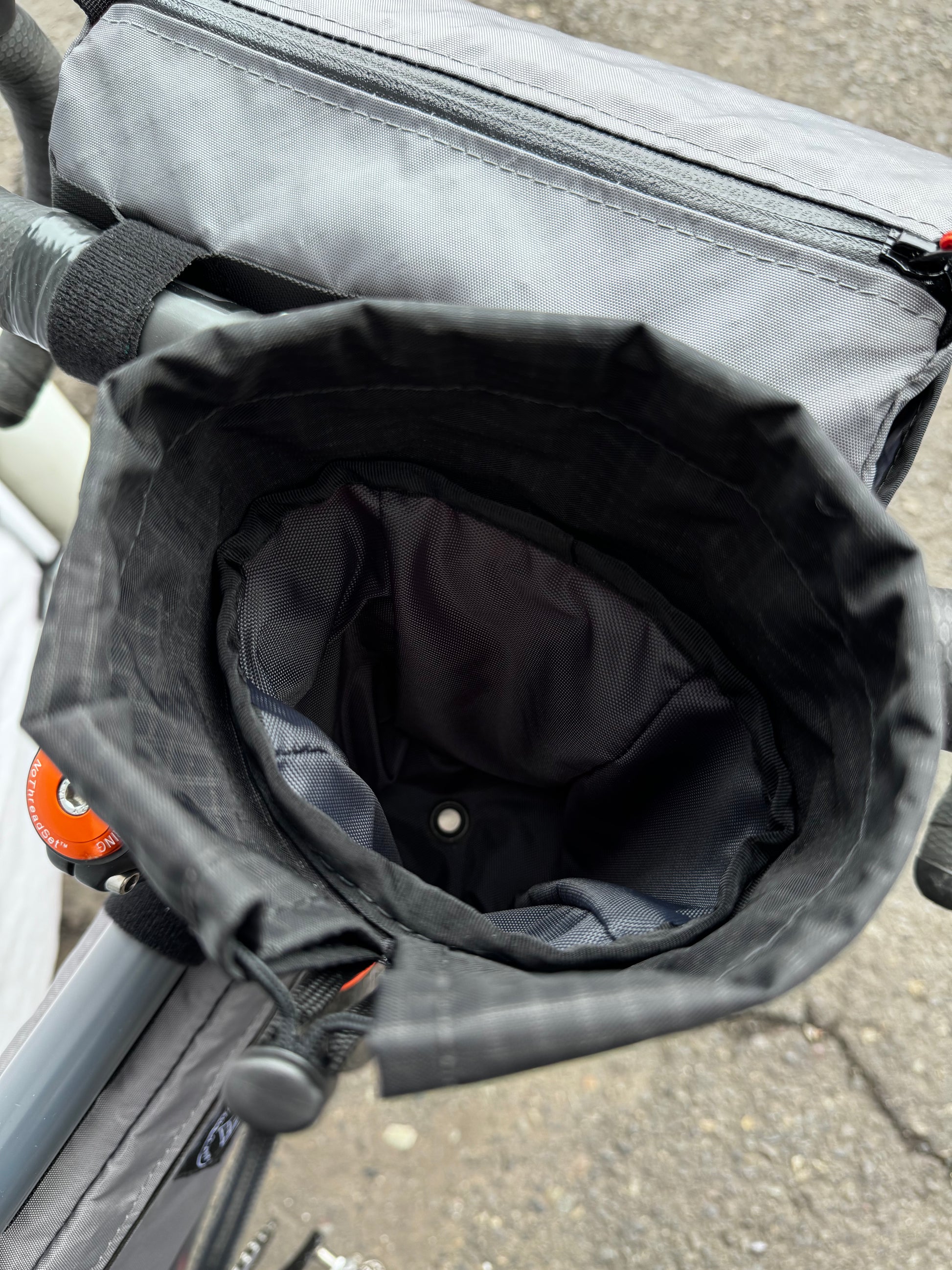 A gray stem bag attached to a bicycle's stem and handlebar, featuring a drawstring closure and made of Ecopak 400 material.  Two external pockets.  Handmade in Portland Oregon USA.